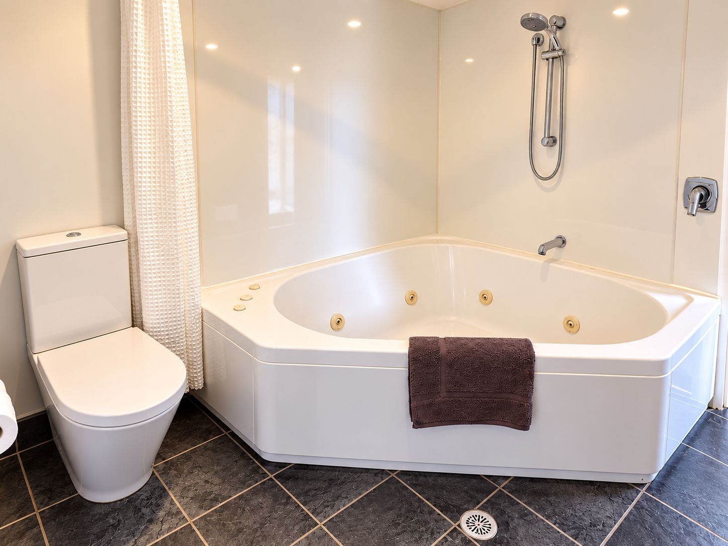 A bathroom with a white toilet, a bathtub with a towel, and a shower head.
