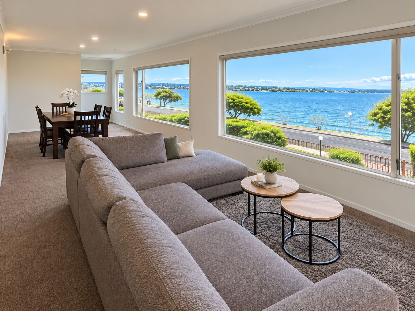 A spacious living area with a large sectional sofa, a dining table with chairs, and a view of the sea through large windows.