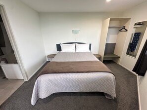 Une chambre d’hôtel bien rangée, avec un grand lit, une petite table de chevet, une chaise, une armoire et un miroir.