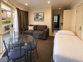 Una habitación de hotel con una mesa de vidrio, sillas, un sofá, una cama y un cuadro en la pared.