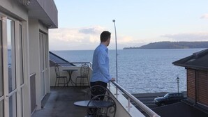 Een balkon met uitzicht op het water, een tafel met stoelen en een auto in de buurt.