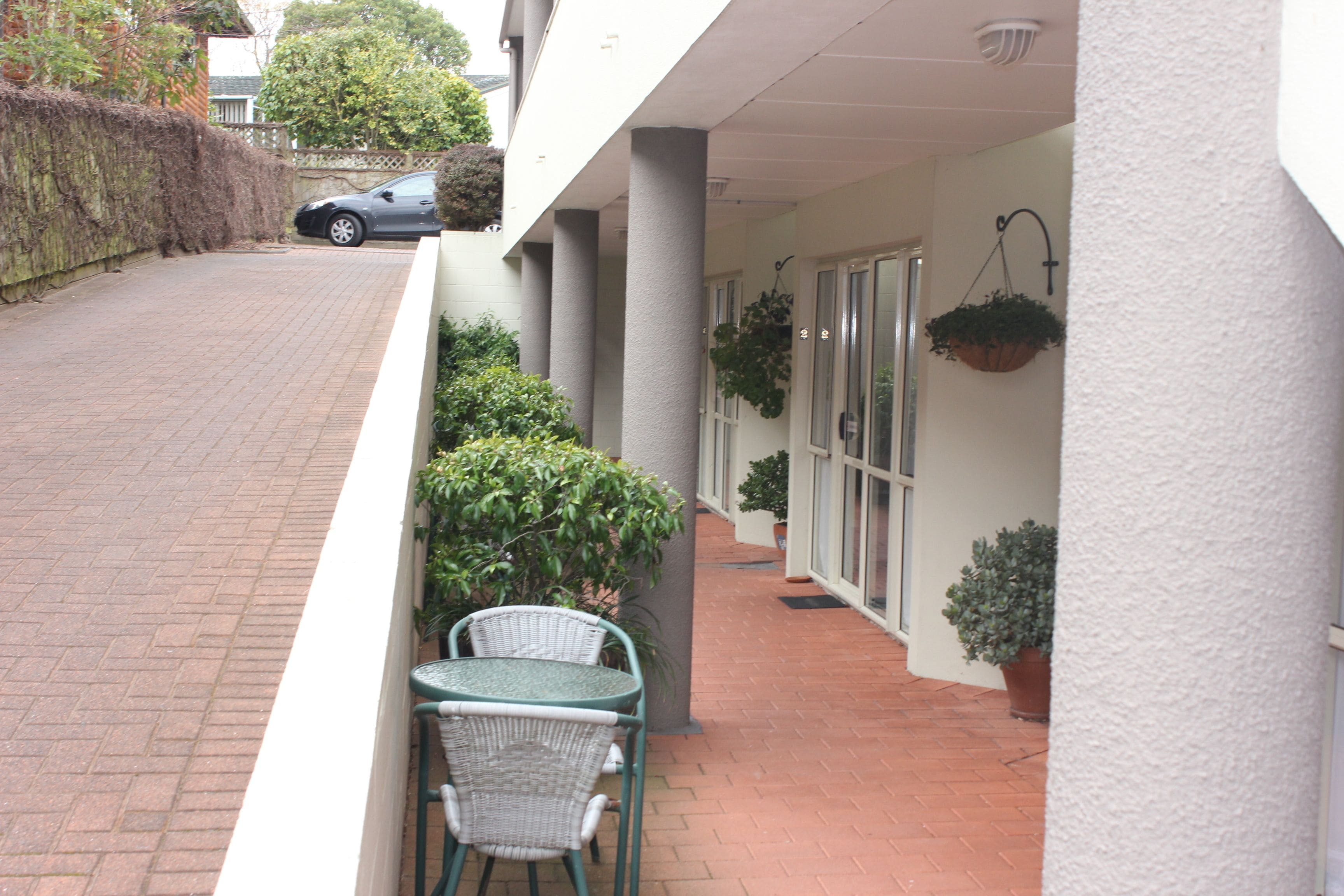 A covered outdoor area with a brick pathway, a table and chairs, and potted plants.