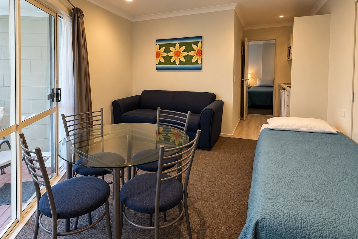 Une pièce de taille modeste, avec une table en verre entourée de chaises, un canapé, un lit et un tableau accroché au mur.