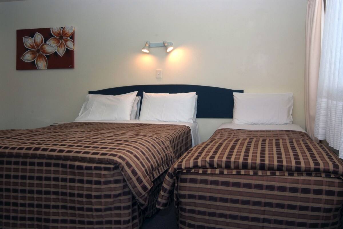 Une chambre d’hôtel avec deux lits, chacun recouvert d’une couvre-lit à carreaux, doté d’une tête de lit et d’un luminaire fixé au mur.