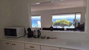 Een keuken met een magnetron, koffiezetapparaat en uitzicht op zee door een raam.