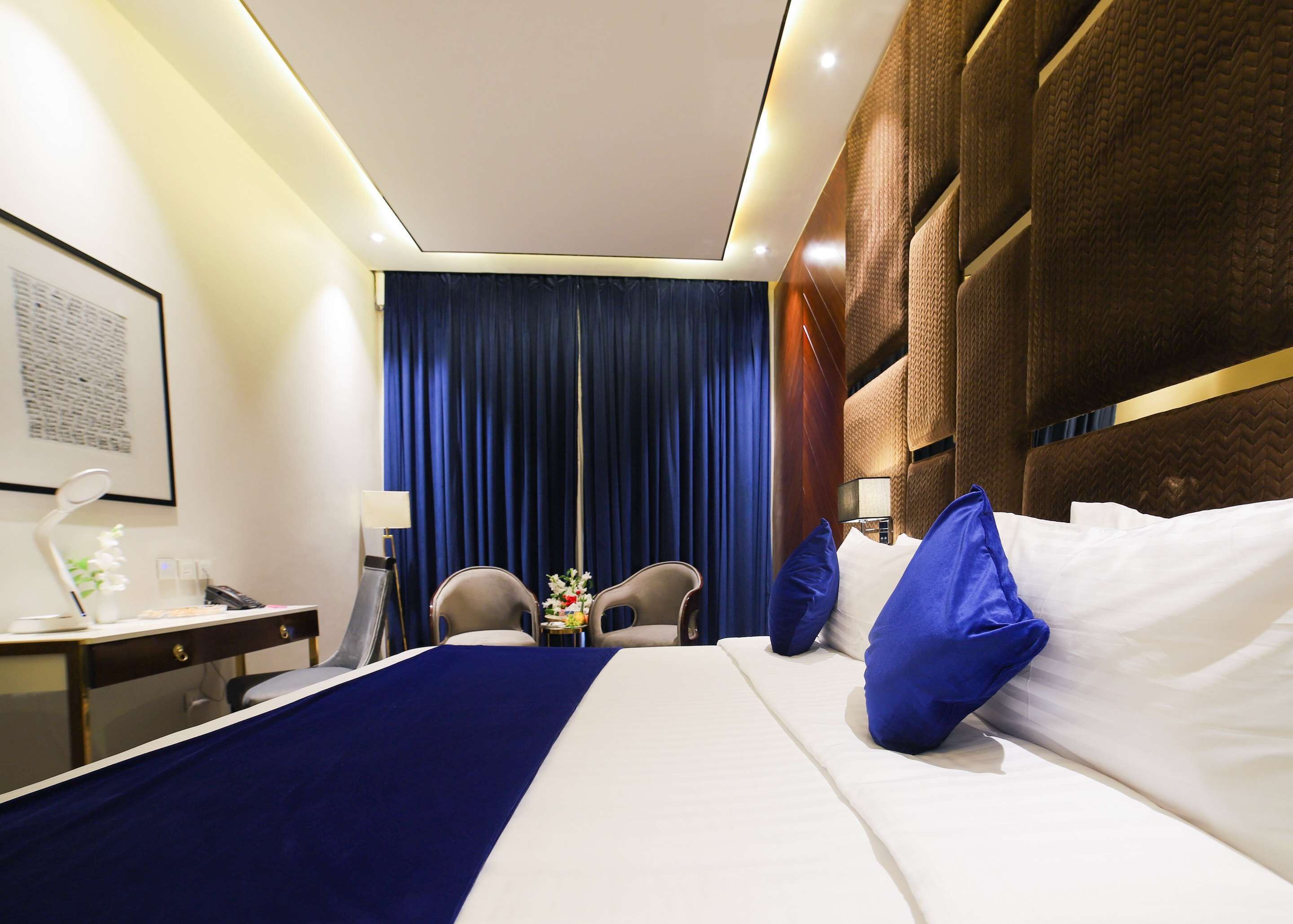 Een hotelkamer met een groot bed, twee stoelen, een bureau met een lamp en een gordijn.