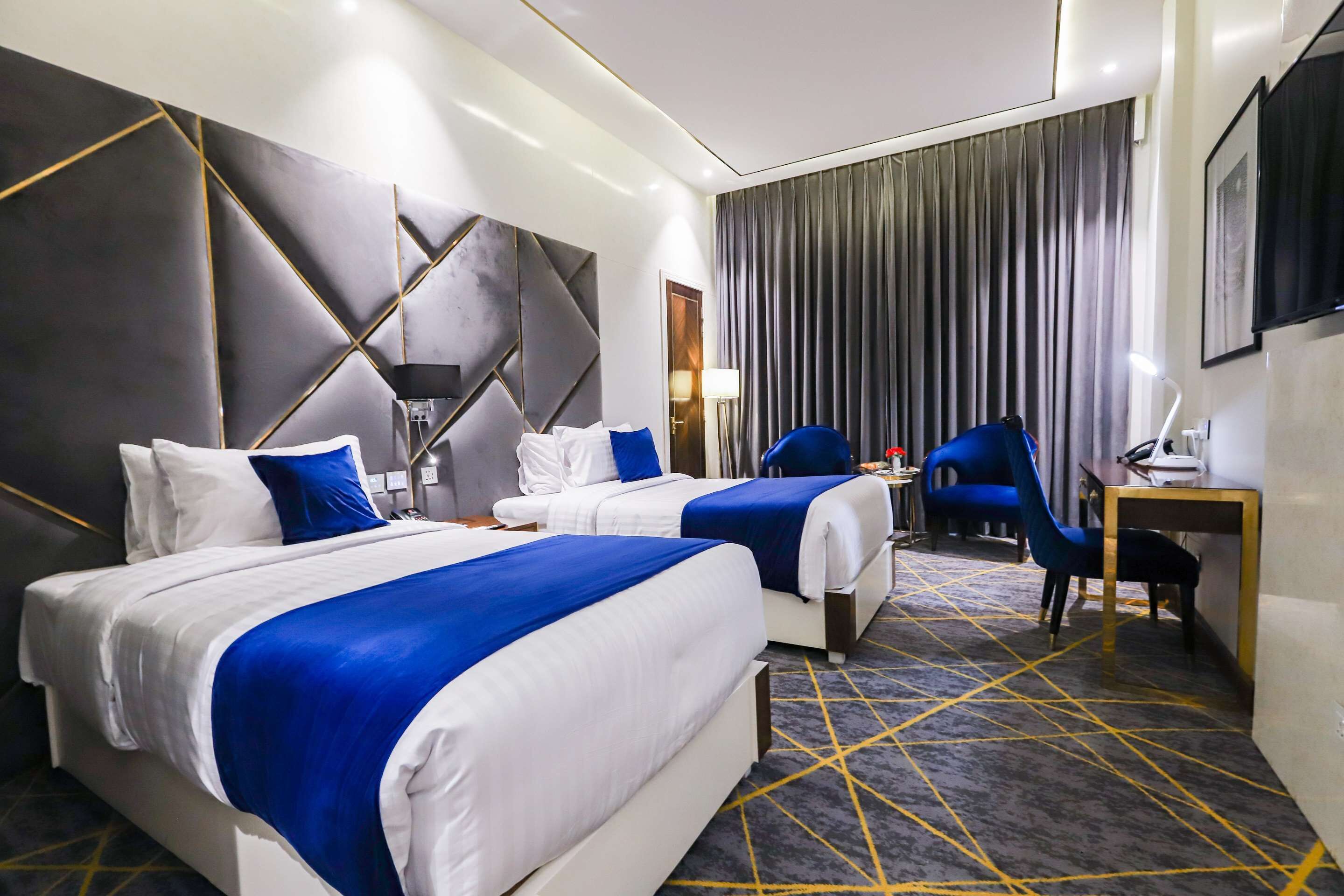 A hotel room with two beds, a desk, a chair, and a large window with curtains.