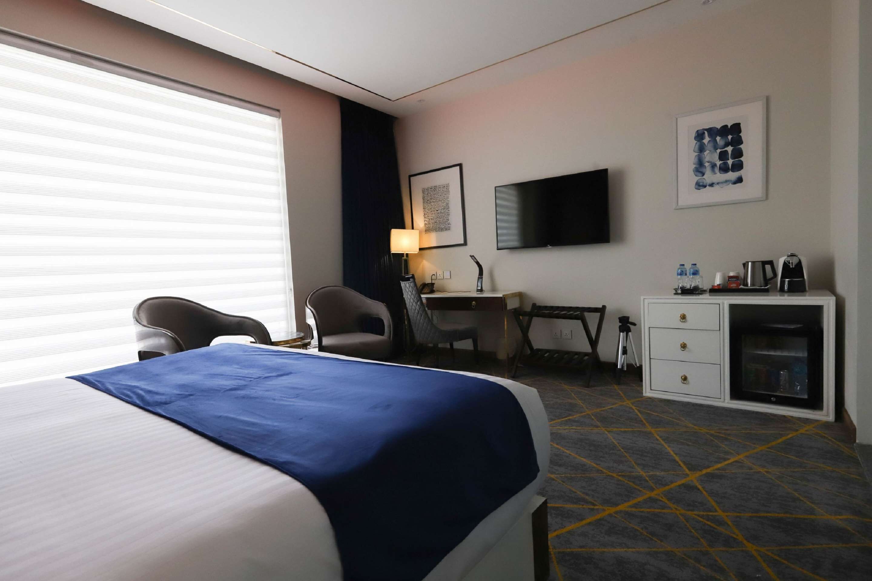 Een hotelkamer met een bed, bureau, stoel, televisie en minibars.