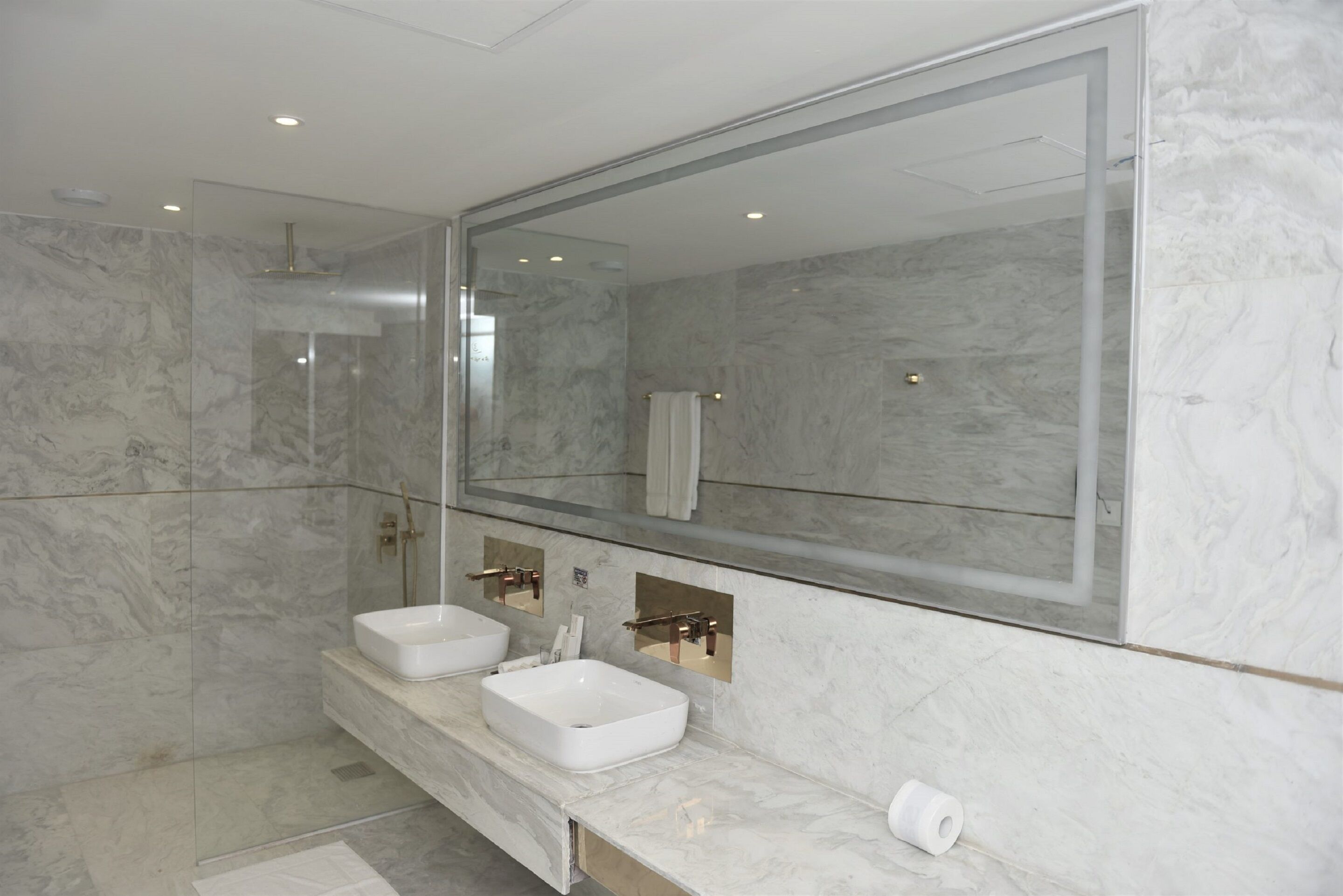 A modern bathroom with two sinks, a large mirror, and marble walls.