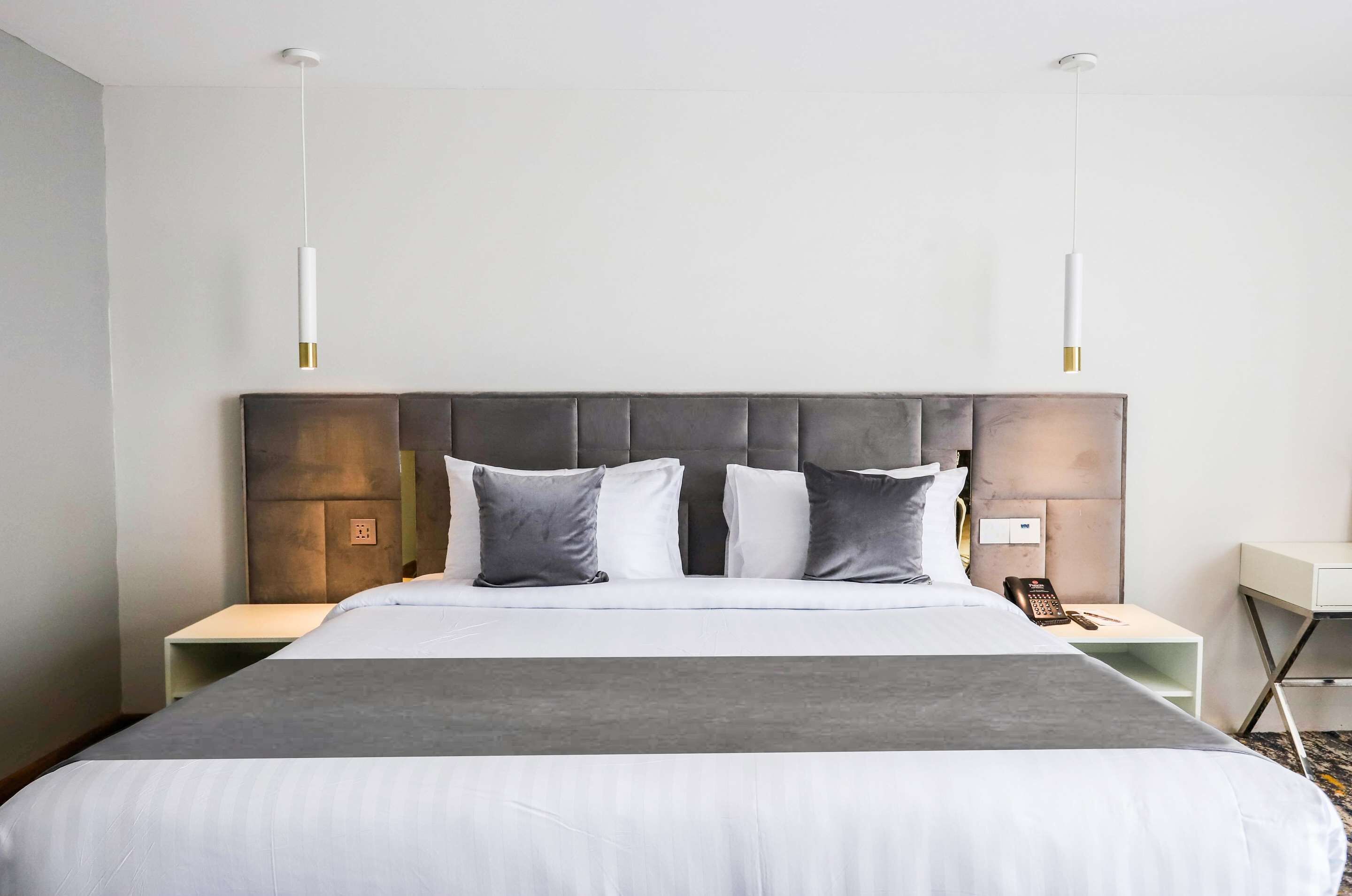 A modern hotel room with a large bed, two bedside tables, and a headboard with a textured design.