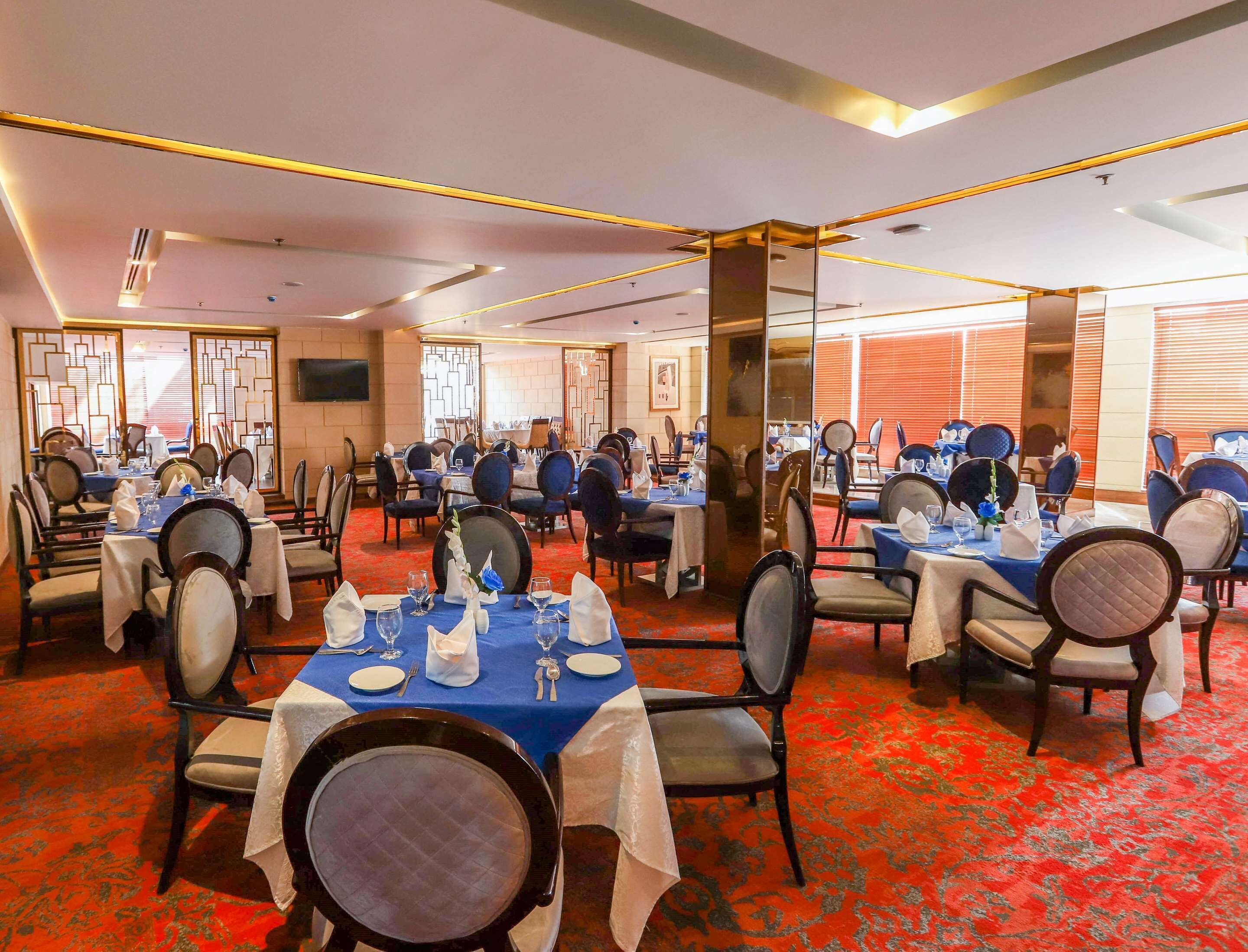 A banquet hall with multiple tables set for dining, featuring a red carpet and modern furnishings.