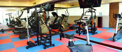 Un gimnasio con diferentes equipos de ejercicio, un televisor montado en la pared y un muro espejado.