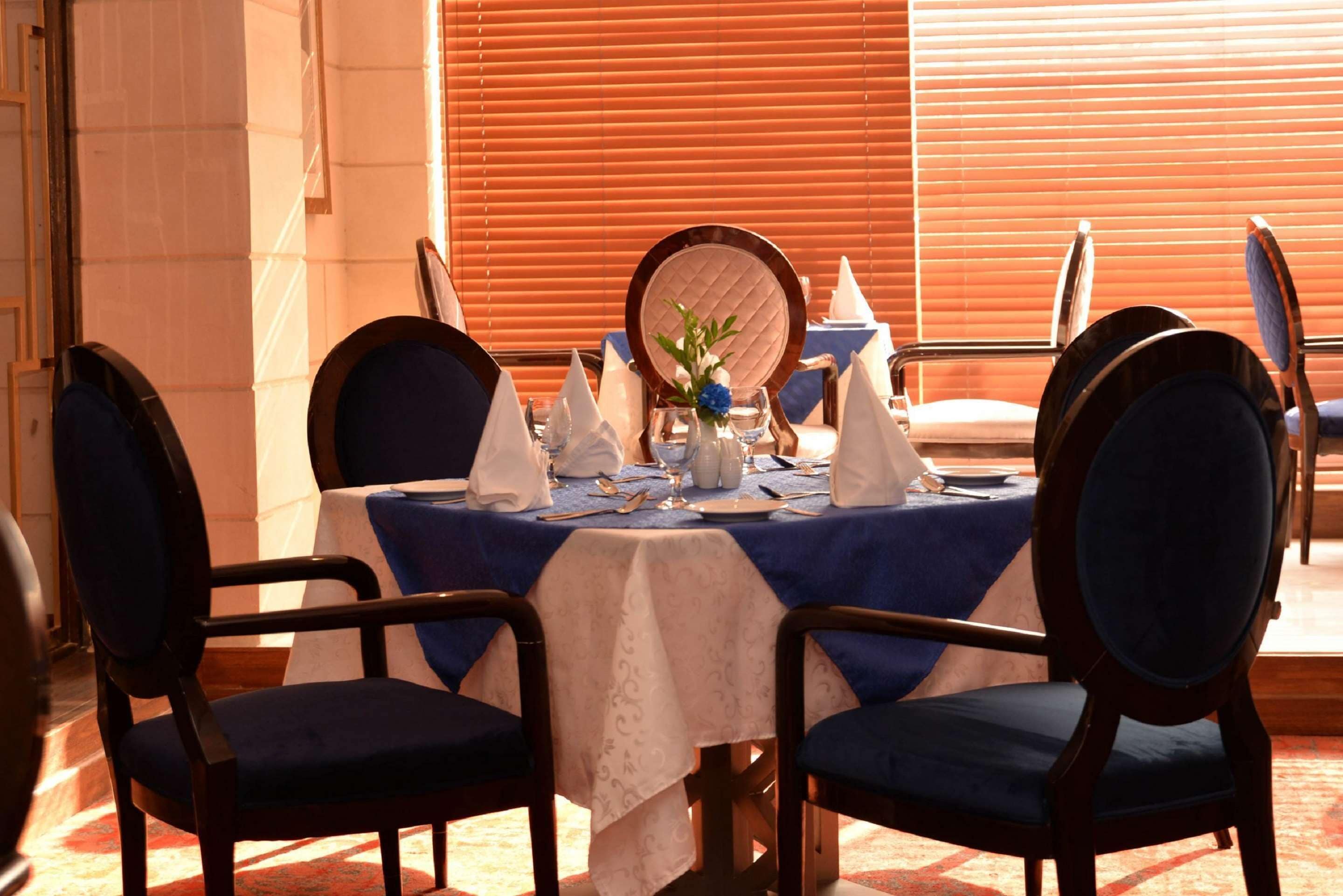 Un comedor con una mesa dispuesta para cuatro personas, con sillas tapizadas en azul y mantel blanco.