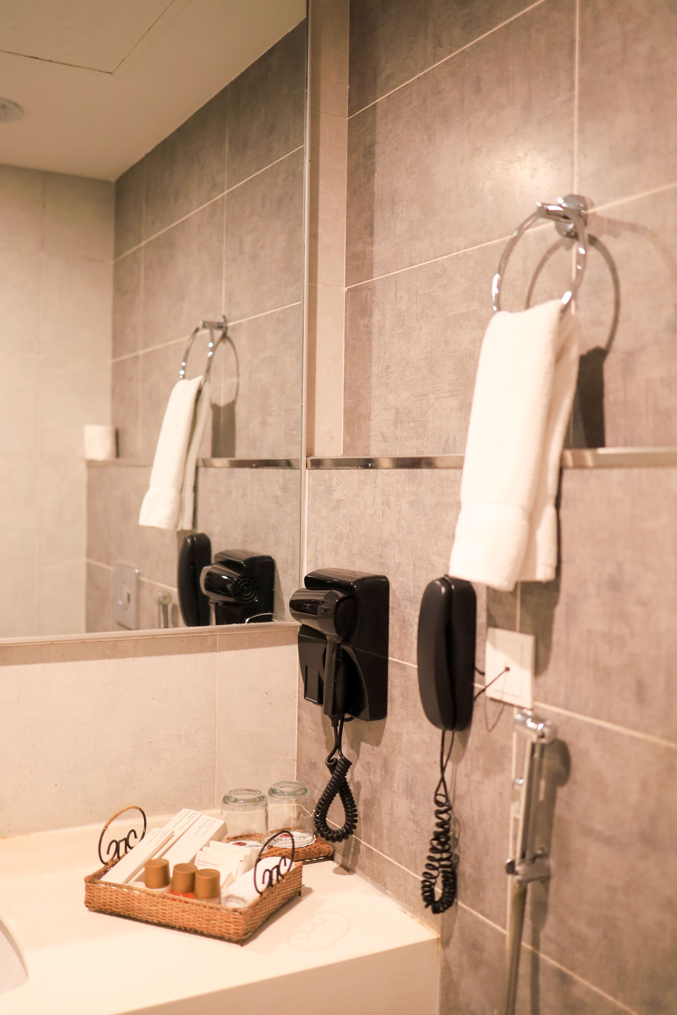 A bathroom with a mirror, a towel rack, a hairdryer, and a telephone.