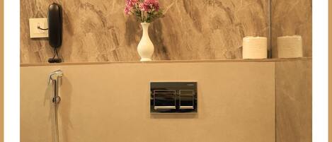 A bathroom with a marble wall, a toilet, a shower, a vase with flowers, and a mirror.