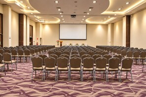 Una sala conferenze con file di sedie, uno schermo per proiettore e pavimento rivestito di moquette.