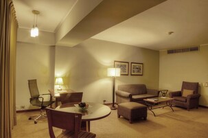 Una habitación de hotel con una mesa de comedor, dos sillones, un sofá, una lámpara y una silla.