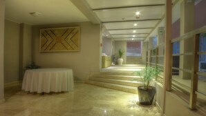 Hall d'albergo con reception, una scala che conduce ai piani superiori e un'ampia opera d'arte a parete.