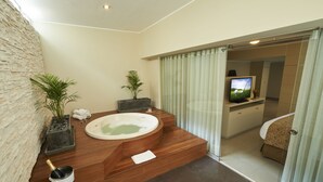 Un bagno moderno con una vasca da bagno in legno, un muro in pietra, una pianta in vaso, un lavandino e un televisore.