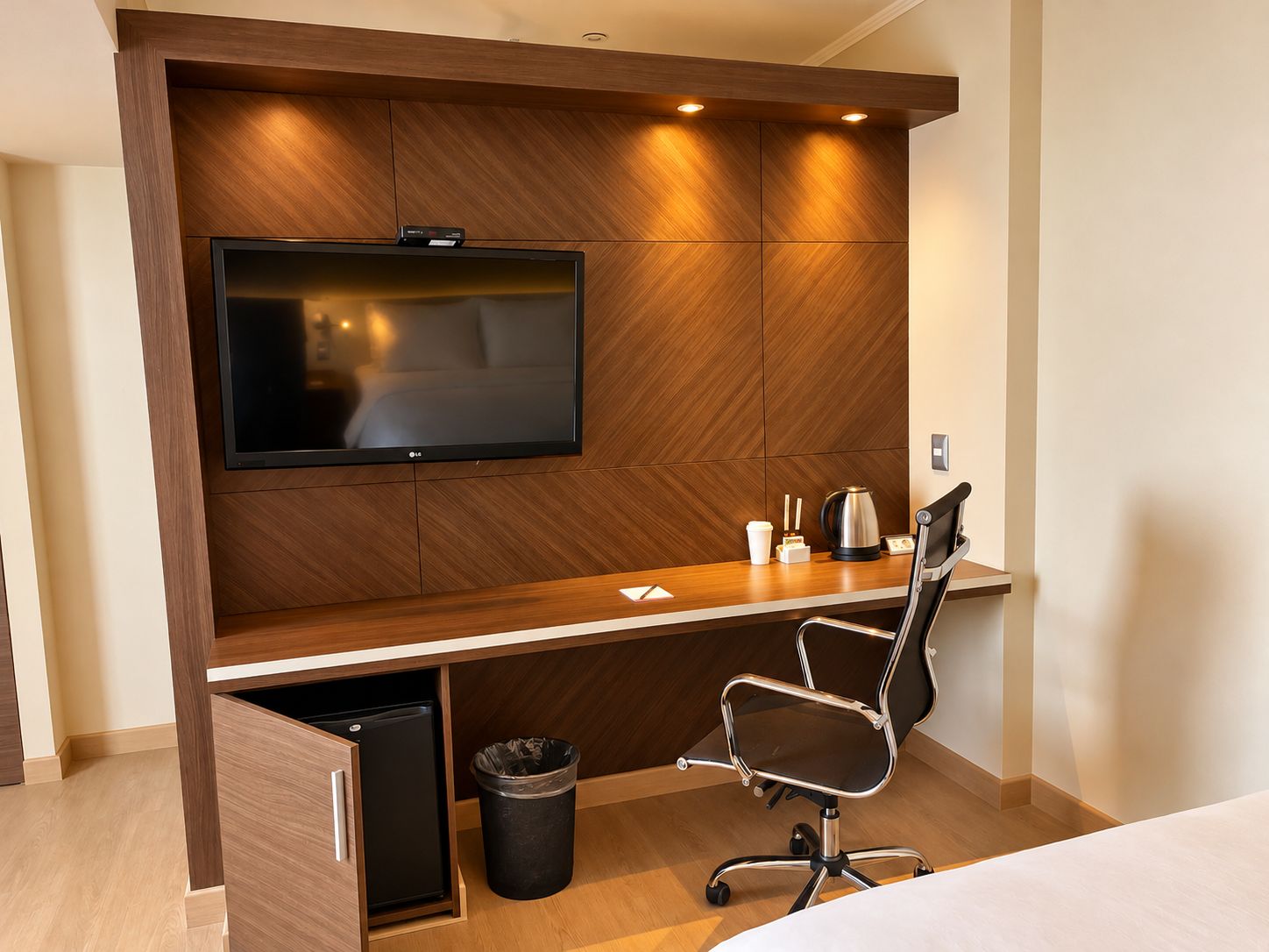 Habitación de hotel con una pared de madera que tiene un televisor de pantalla plana, un escritorio con una silla, una cafetera y un cesto de basura.