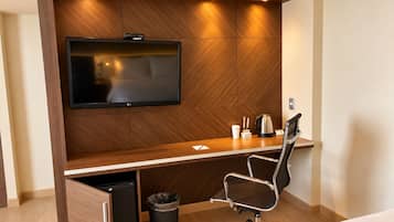 Habitación de hotel con una pared de madera que tiene un televisor de pantalla plana, un escritorio con una silla, una cafetera y un cesto de basura.