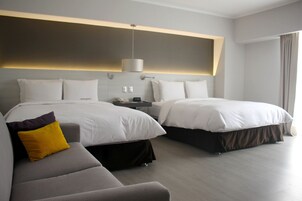 A modern hotel room with two beds, a sofa, and a bedside table.