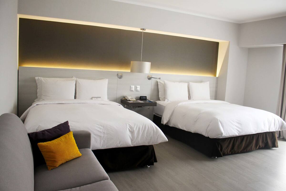Una habitación de hotel con dos camas, un sofá, una mesita de noche y una lámpara.