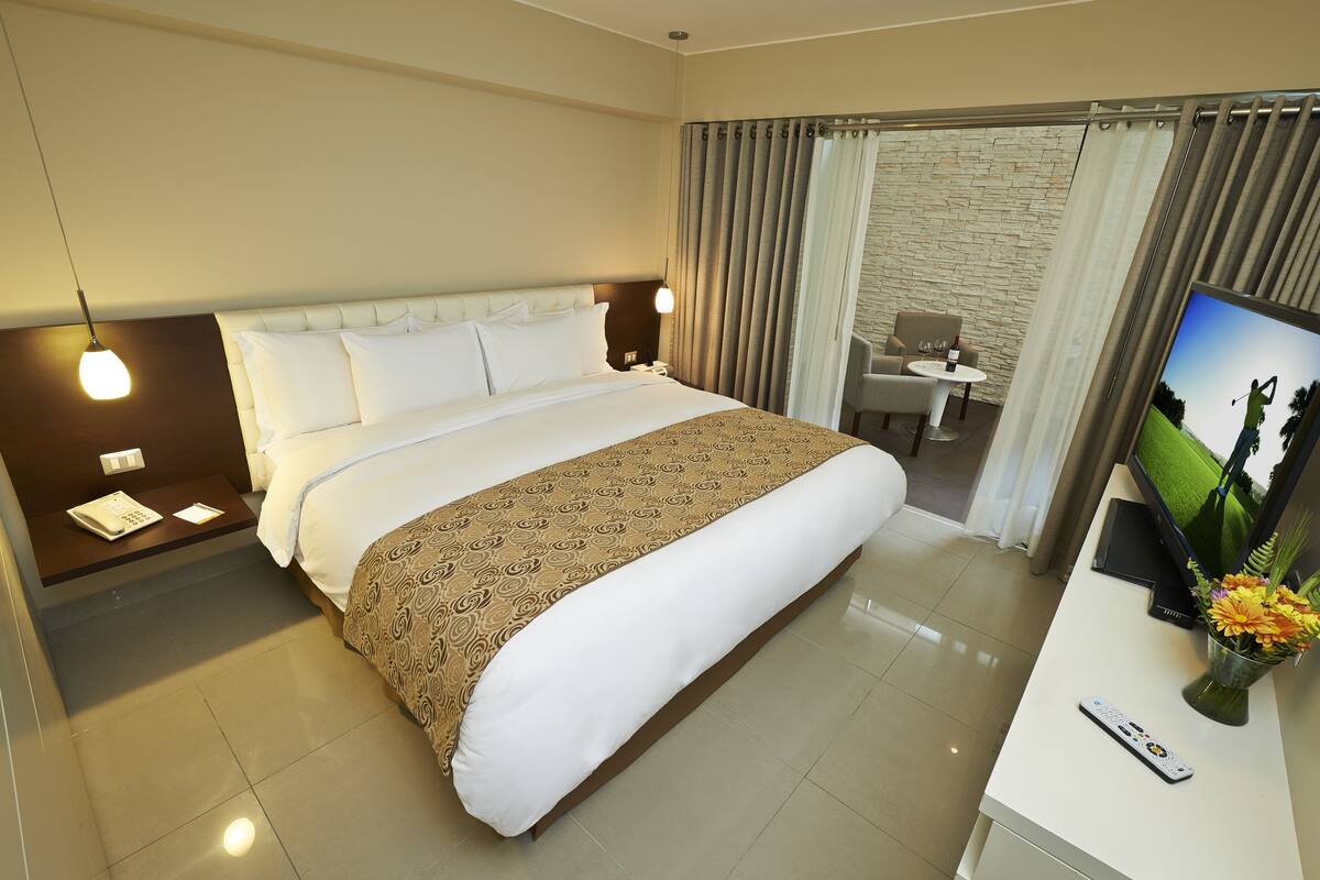 Una habitación de hotel con una cama grande, un escritorio con una silla, un televisor y un jarrón con flores.