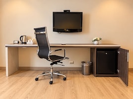 A modern office space with a desk, chair, TV, and a small trash bin.