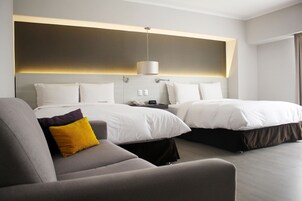 A modern hotel room with two beds, a sofa, and a bedside table with a lamp.