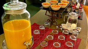 Un'area buffet con un distributore automatico di succo d'arancia, ciotole di frutta e diversi condimenti.