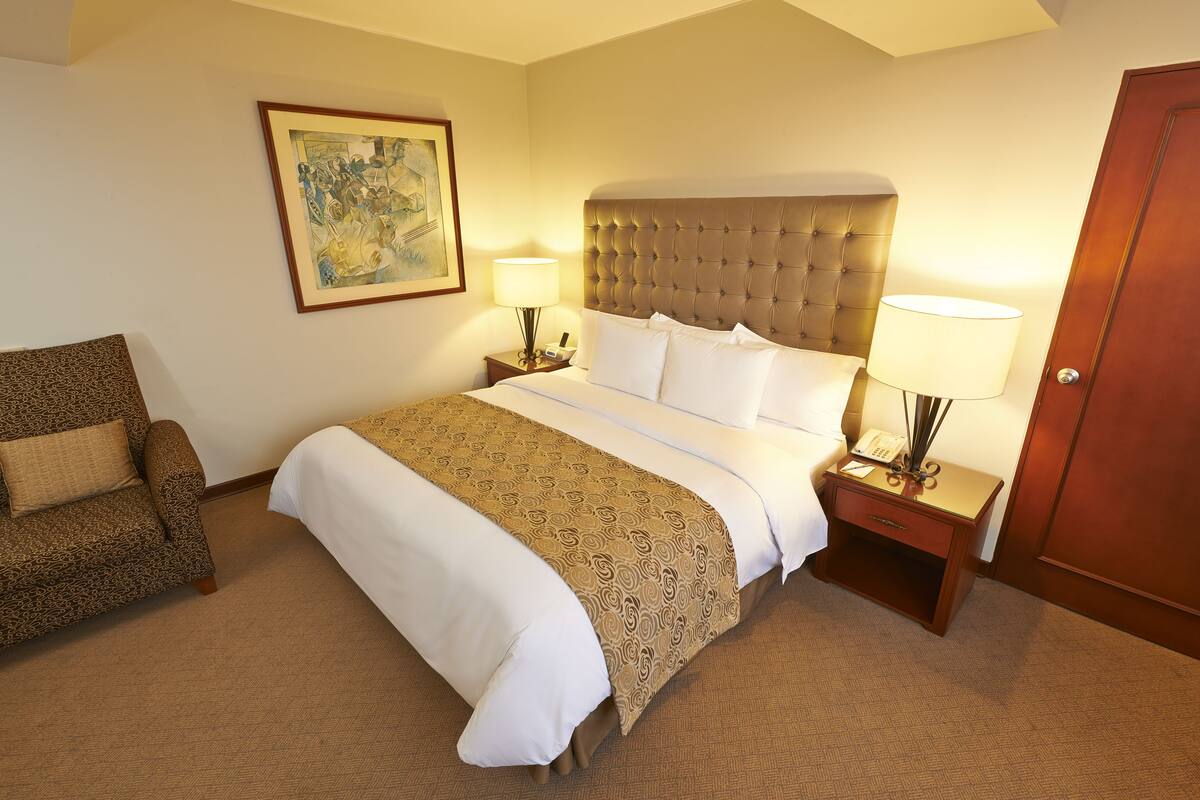 Una habitación de hotel con una cama grande, dos mesitas de noche, una silla y una puerta.