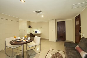 A modern living room with a dining area, a sofa, and a small kitchen area with a laptop on the counter. - Sol de Oro Hotel & Suites (Lima)