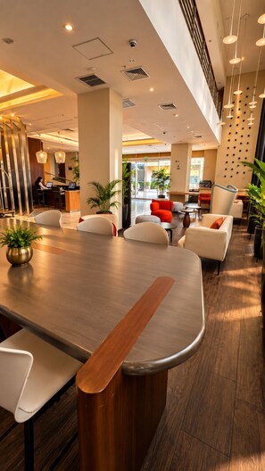 Una hall moderna di un hotel con un lungo tavolo da conferenze, zona salotto con sedie e una reception.