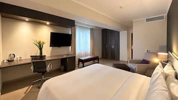 Ett hotellrum med en stor säng, ett skrivbord med en platt-TV, en sittgrupp med en bänk och en garderob.