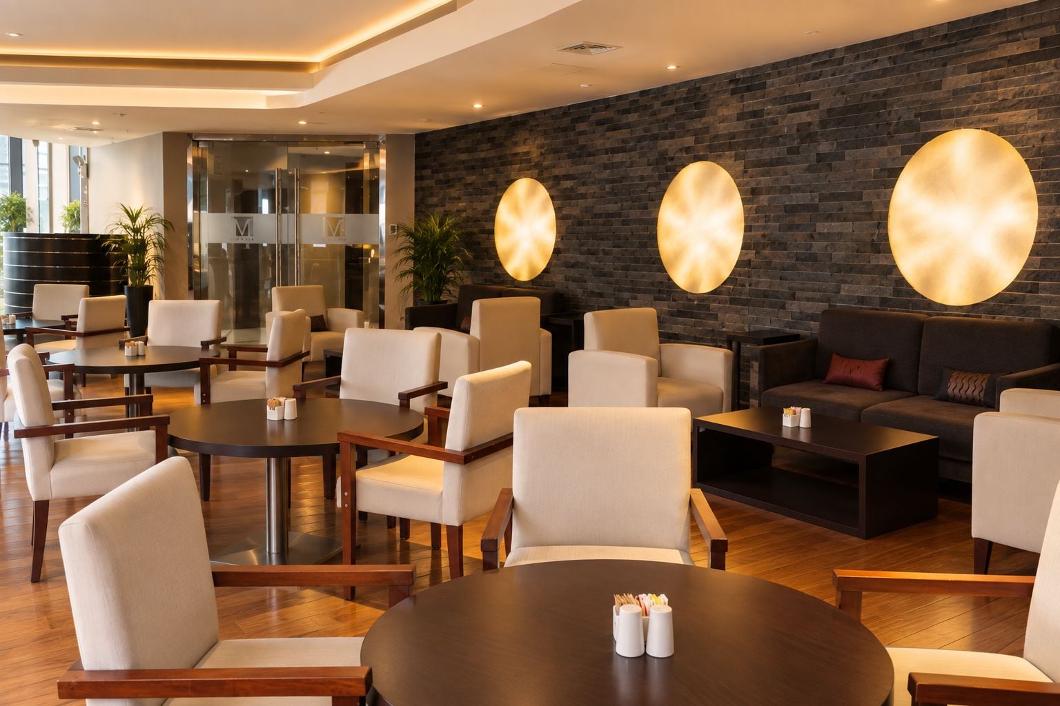 A modern hotel lobby with round tables, comfortable seating, a brick wall, and a glass entrance.