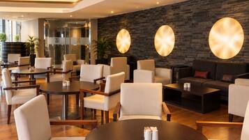 A modern hotel lobby with round tables, comfortable seating, a brick wall, and a glass entrance.