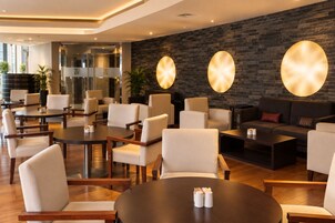 A modern hotel lobby with round tables, comfortable seating, a brick wall, and a glass entrance.