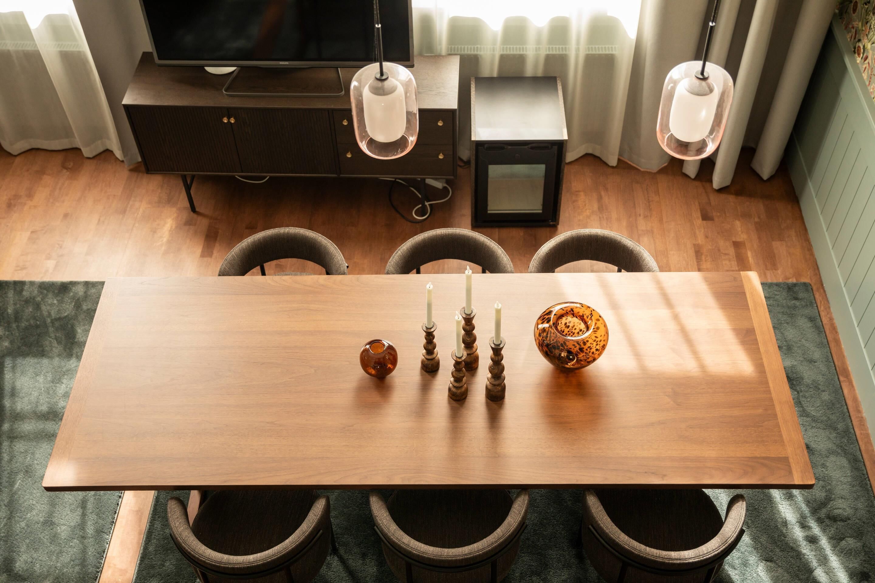 Uma área de jantar com mesa de madeira, quatro cadeiras, velas e uma tigela decorativa.