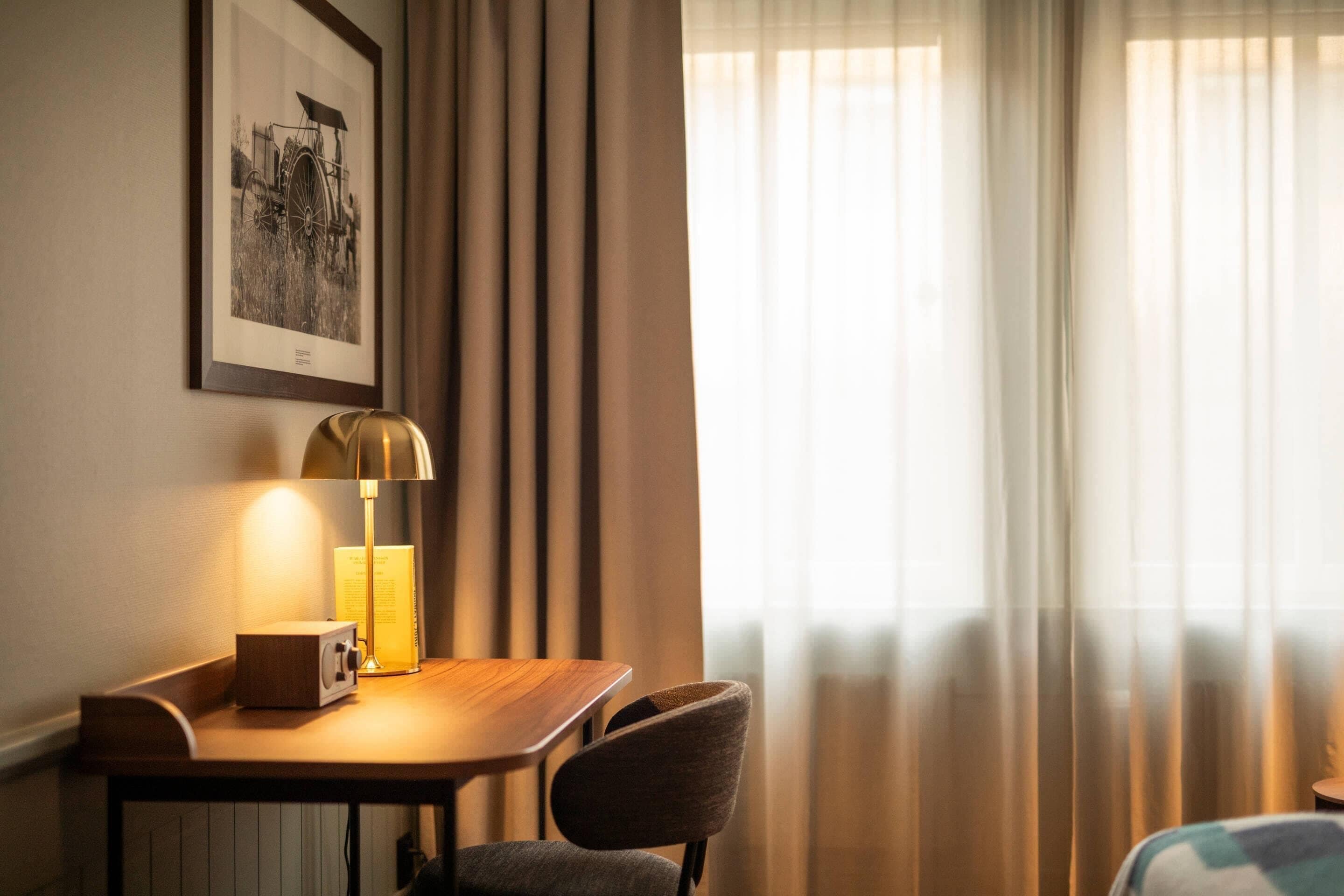 Habitación de hotel con una mesa de madera, una silla, una lámpara y un cuadro en la pared.