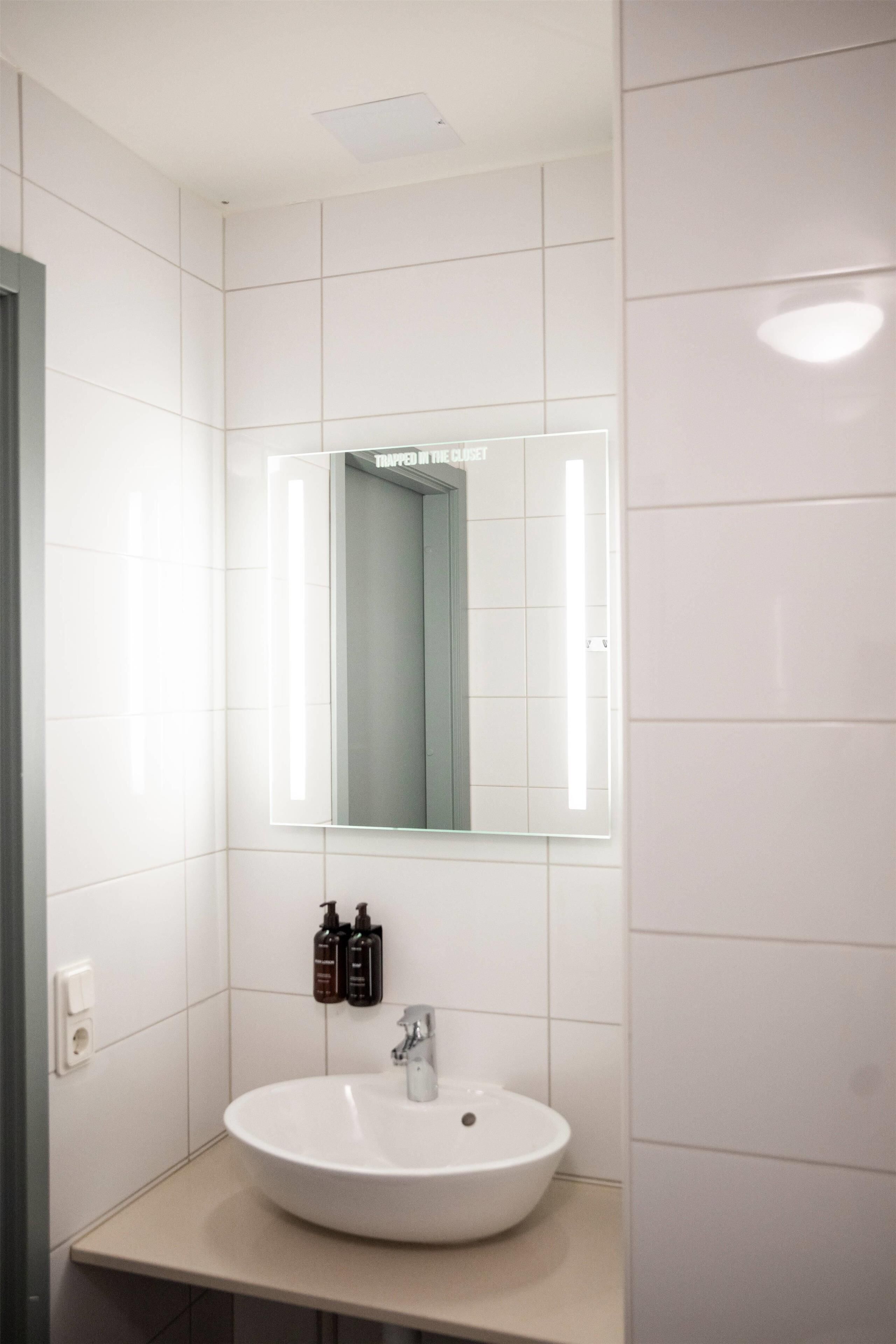 Un baño moderno con un lavamanos blanco, un espejo y una lámpara sobre él.