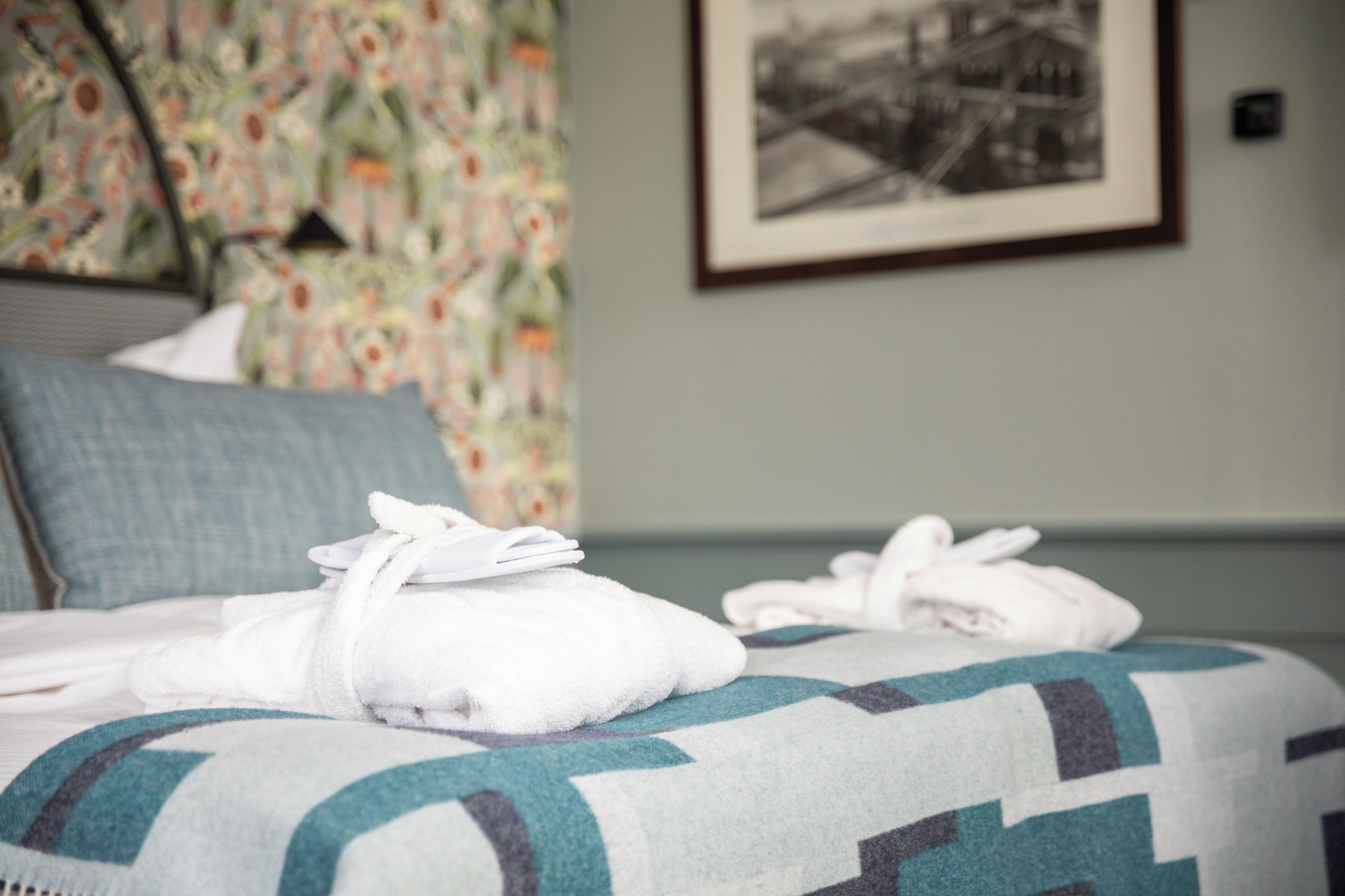 Una cama bien hecha con una colcha estampada, una pared cubierta de papel tapiz floral y un cuadro en la pared.