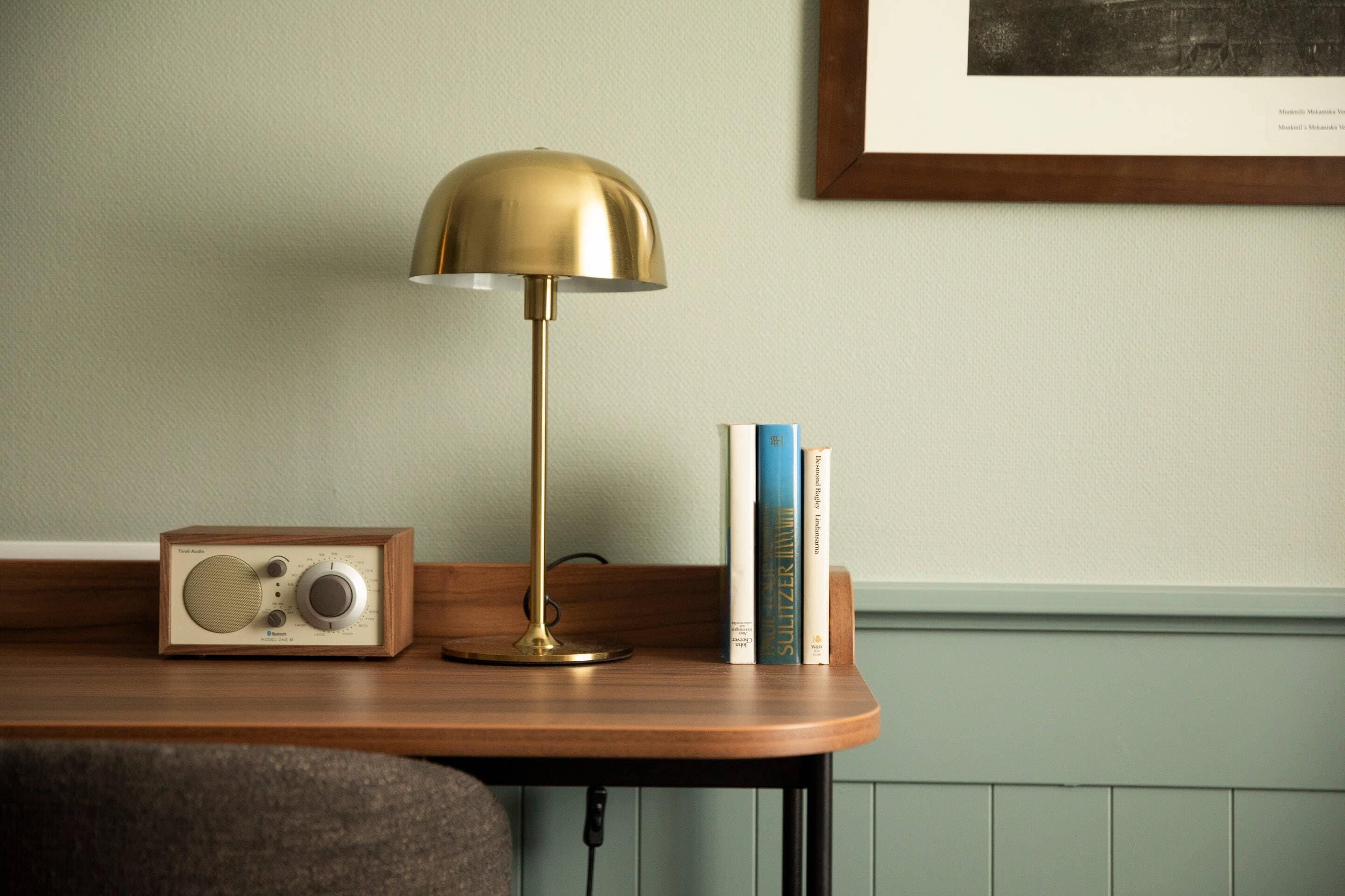 A wooden desk with a vintage radio, a brass desk lamp, and a stack of books.