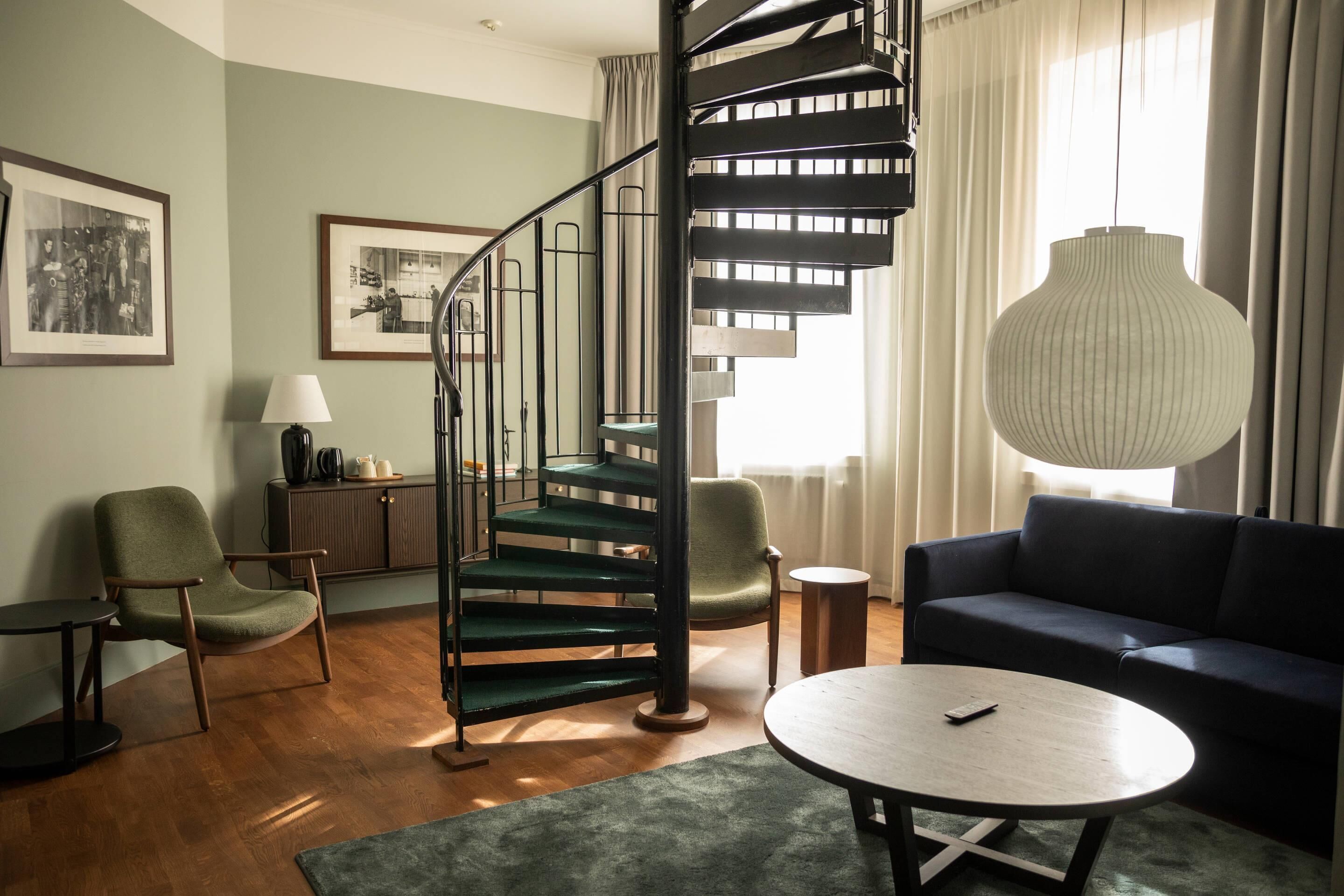 Una sala de estar moderna con una escalera en espiral, un sofá, una mesa redonda de centro y una lámpara.