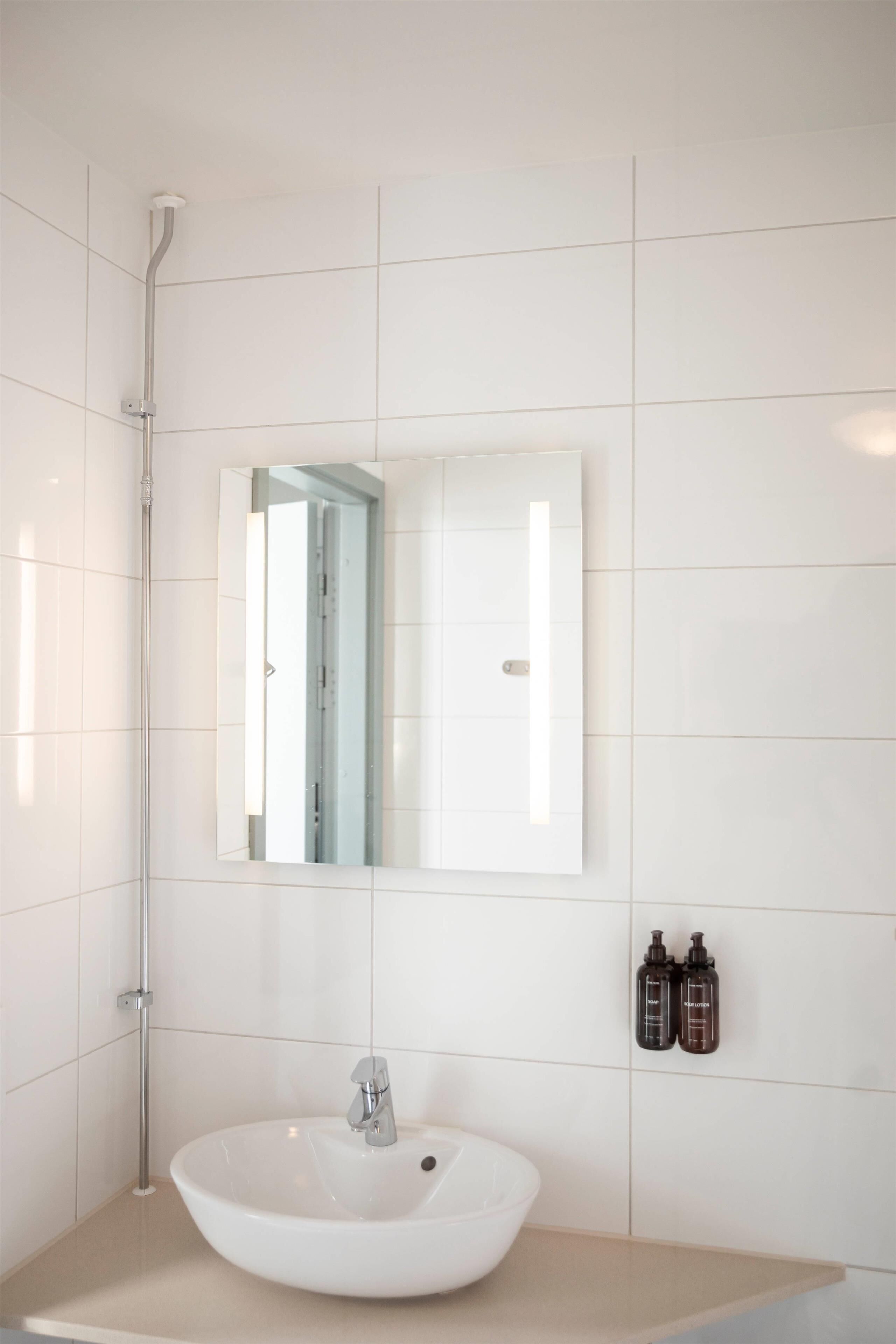 Ein modernes Badezimmer mit einem weißen Waschbecken, einem Spiegel und zwei Shampooflaschen an der Wand.