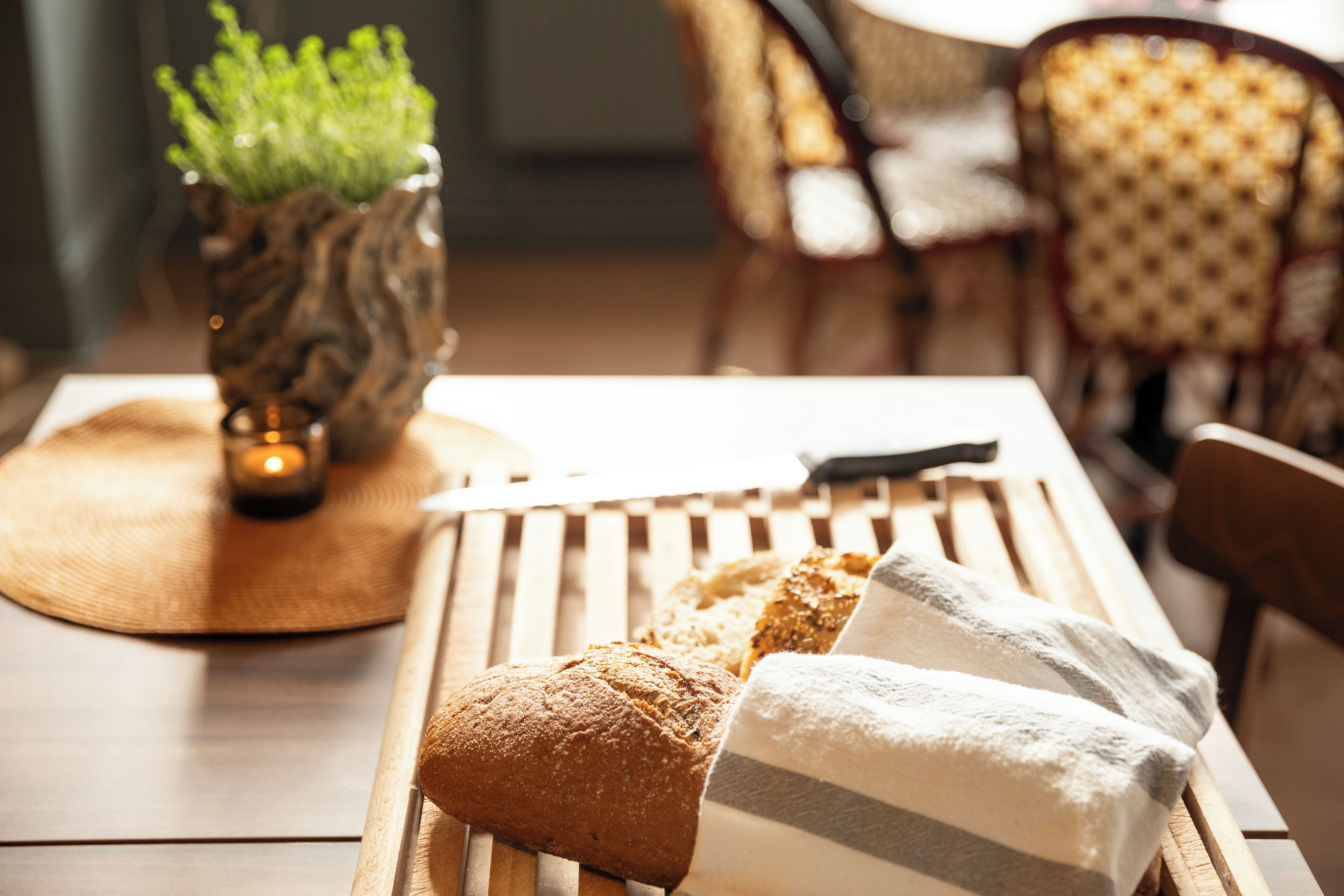 A wooden table with bread and a cloth napkin, a vase with a plant, and a candle.