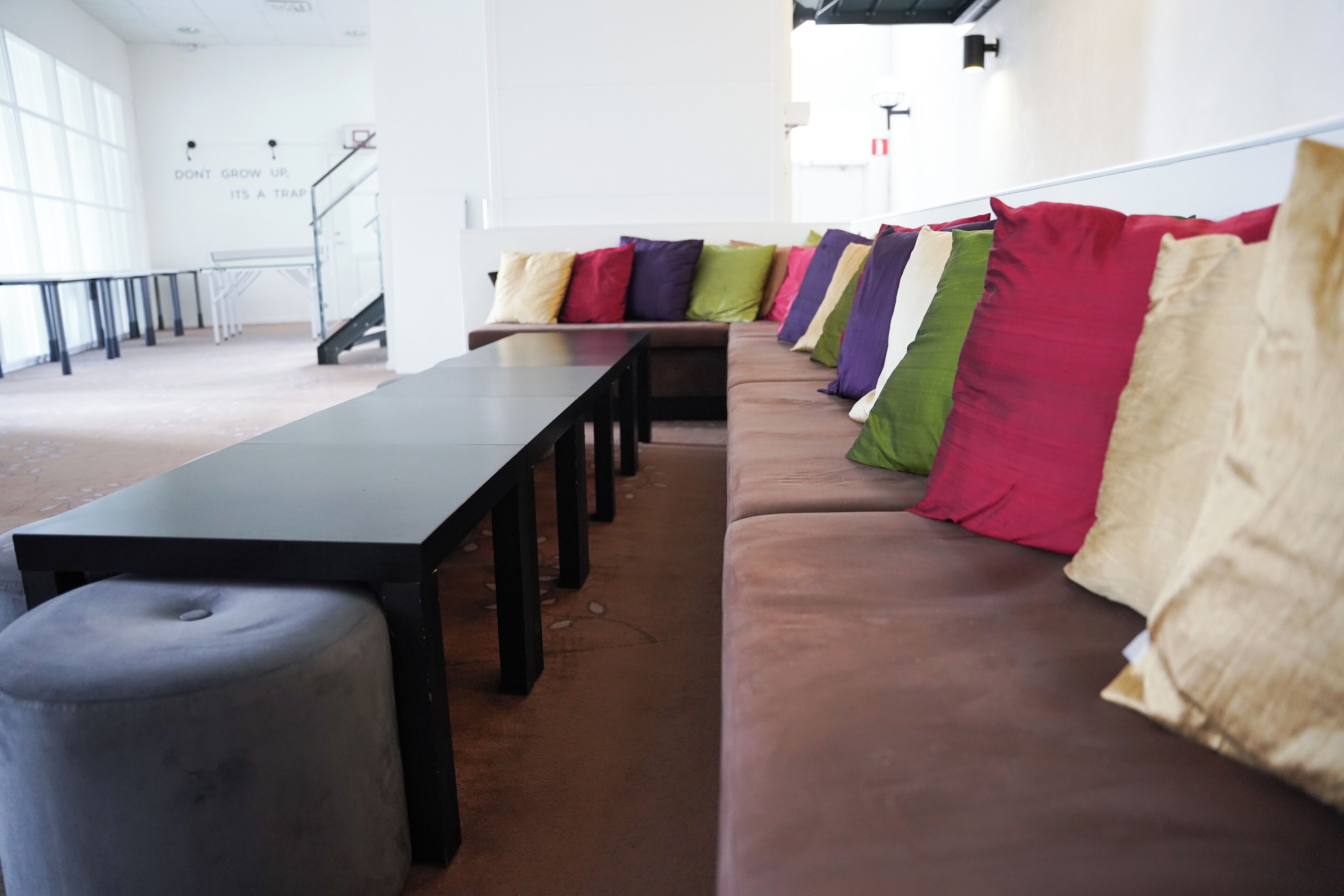 A modern interior with a long black table, a brown sofa with colorful cushions, and a staircase in the background.