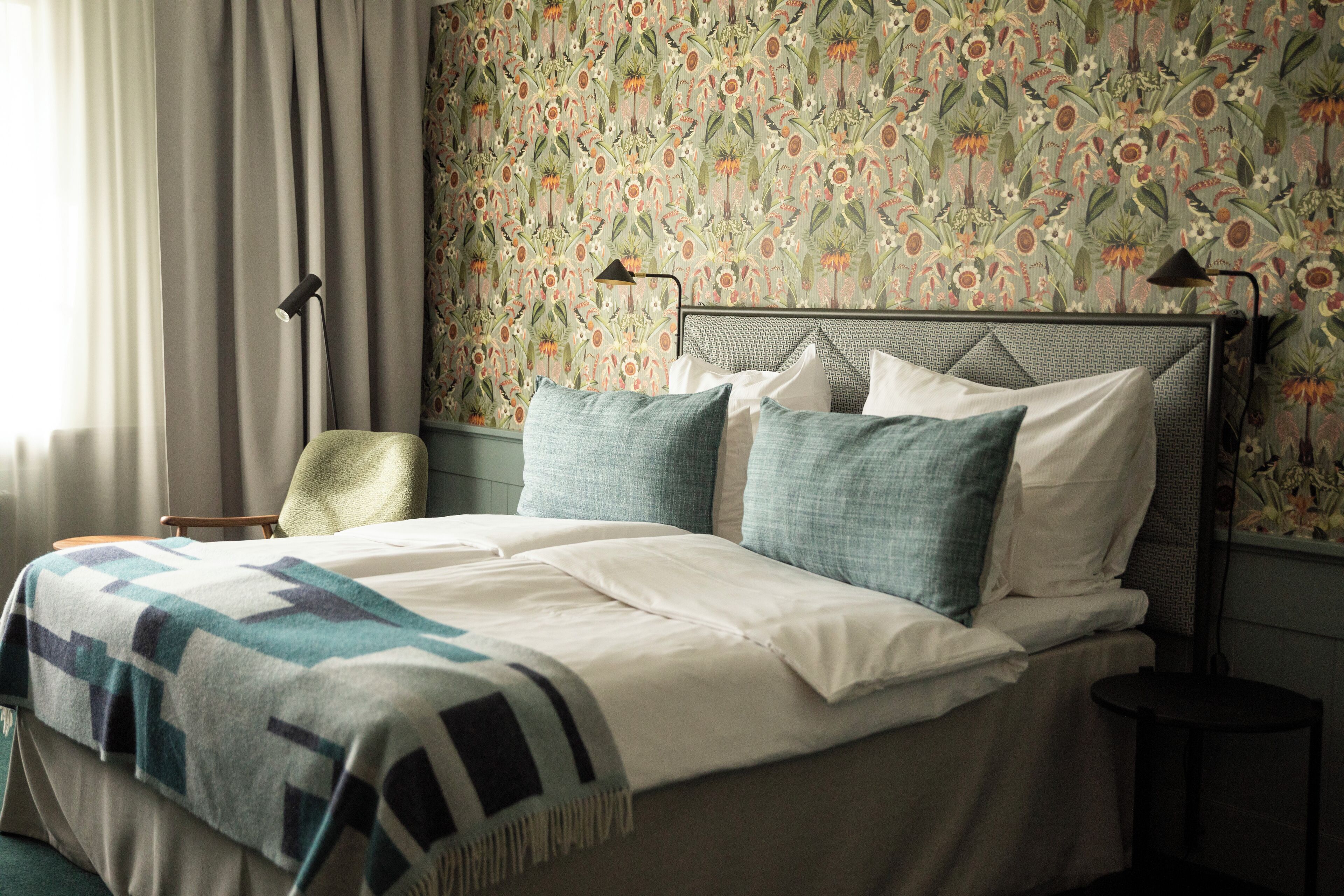 A neatly made bed with a patterned blanket, a headboard, and two bedside lamps.