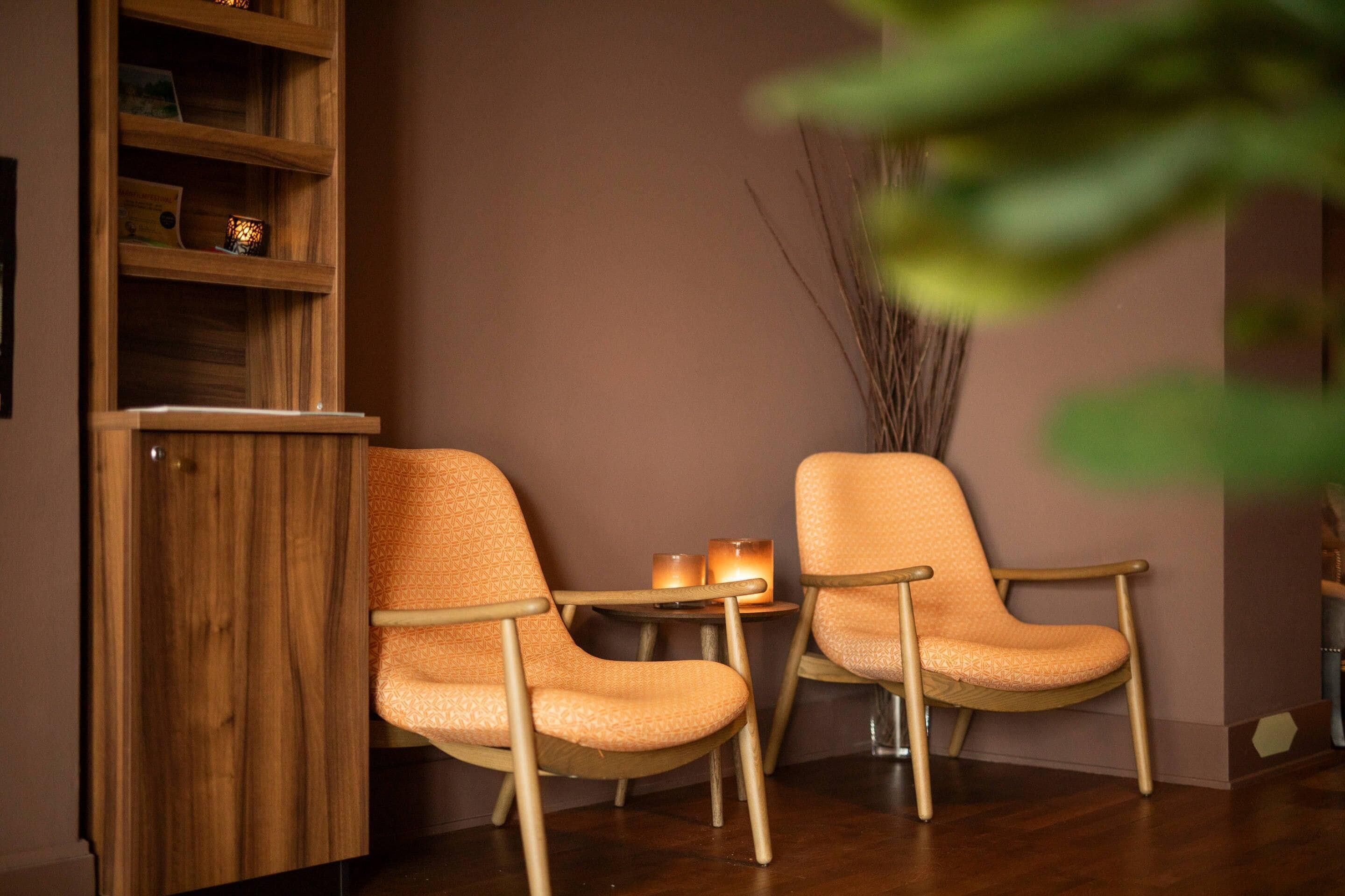 A room with two orange patterned chairs, a wooden cabinet, and a small table with candles.