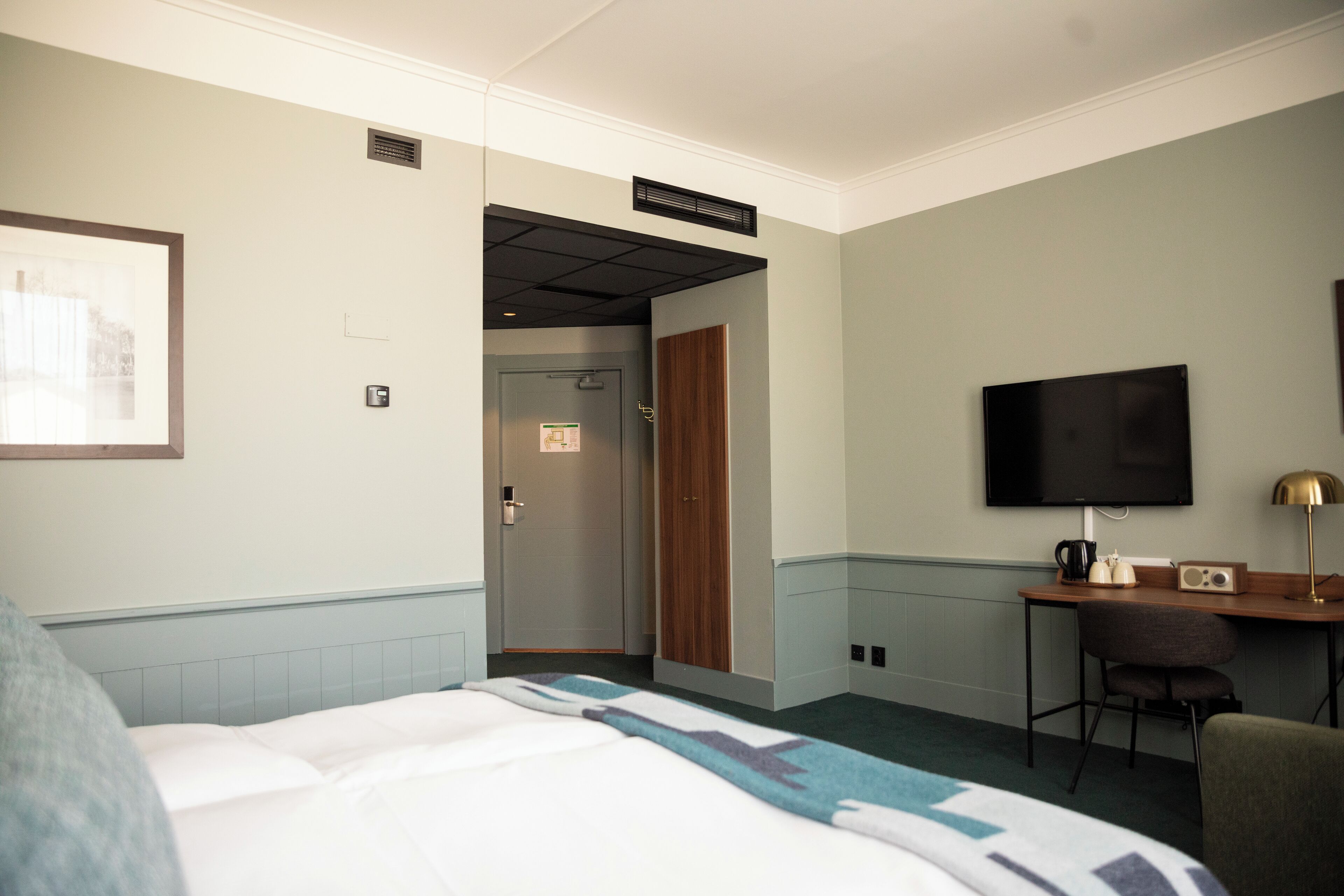 A hotel room with a bed, a desk with a chair, a television, and a door leading to a bathroom.